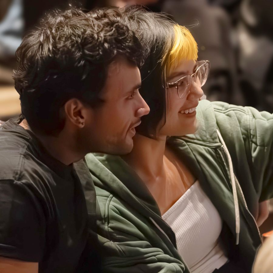 A young man and woman sit together in the theatre with the woman pointing toward the stage.