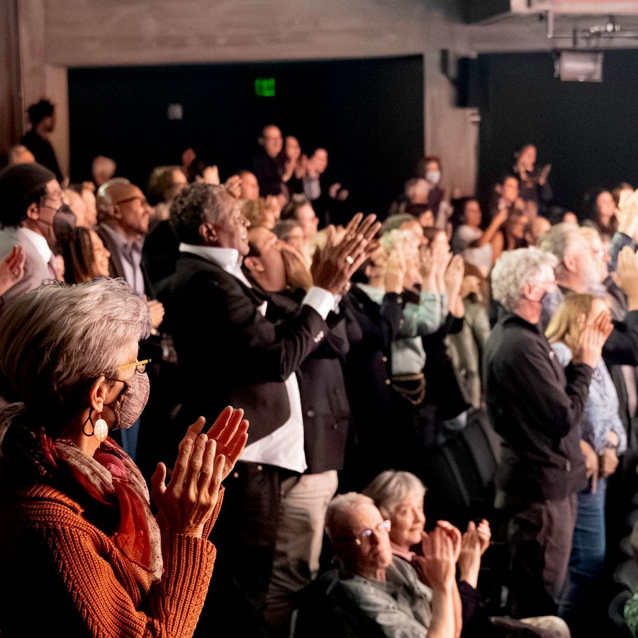 A packed theatre audience gives an enthusiastic standing ovation.
